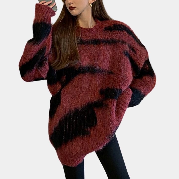 Vrouw in oversized rood-zwarte gebreide trui met abstract patroon, draagt zwarte legging. Modieuze winterkleding, trendy damesmode.