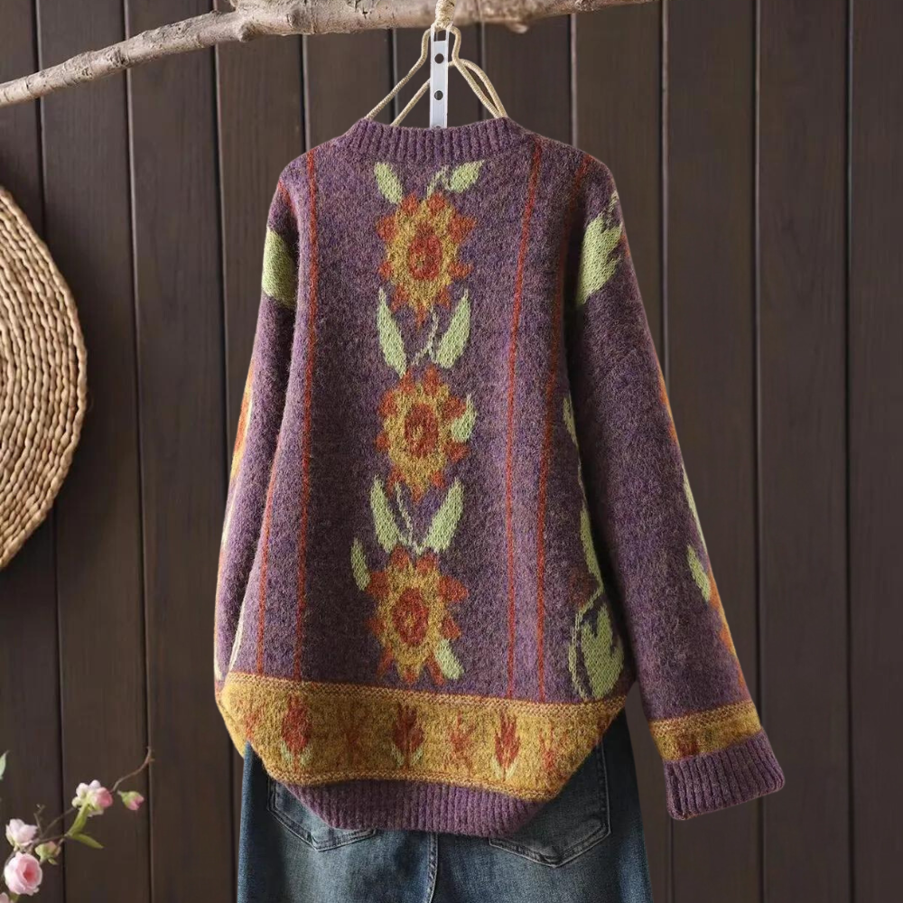 Paarse gebreide trui met zonnebloemmotief, hangend aan een houten hanger. Perfect voor herfstmode, warme kleding, vintage stijl.
