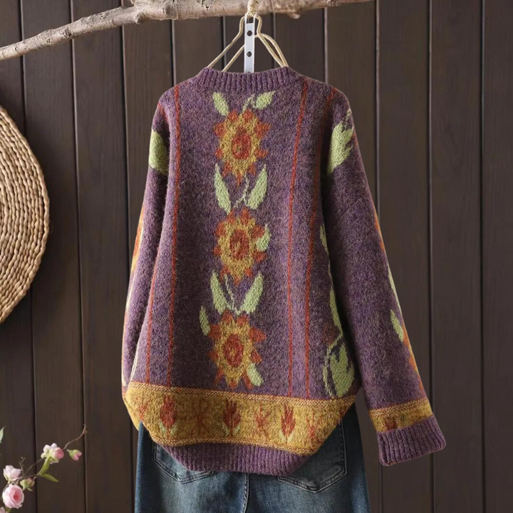 Paarse gebreide trui met zonnebloemmotief, hangend aan een houten hanger. Perfect voor herfstmode, warme kleding, vintage stijl.