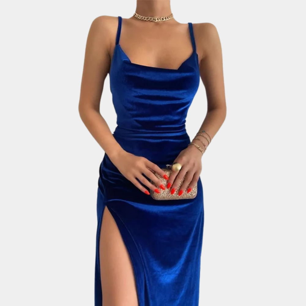 Blauwe fluwelen damesjurk met spaghettibandjes en hoge split, gecombineerd met gouden sieraden en een glinsterende clutch. Perfect voor avondkleding.