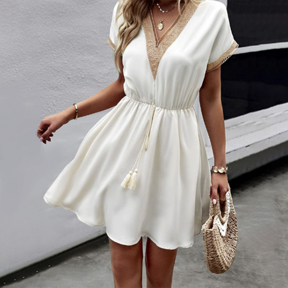 Vrouw in elegante witte zomerjurk met V-hals en kanten details, draagt een strooien tas. Perfecte outfit voor casual en zomerse gelegenheden.
