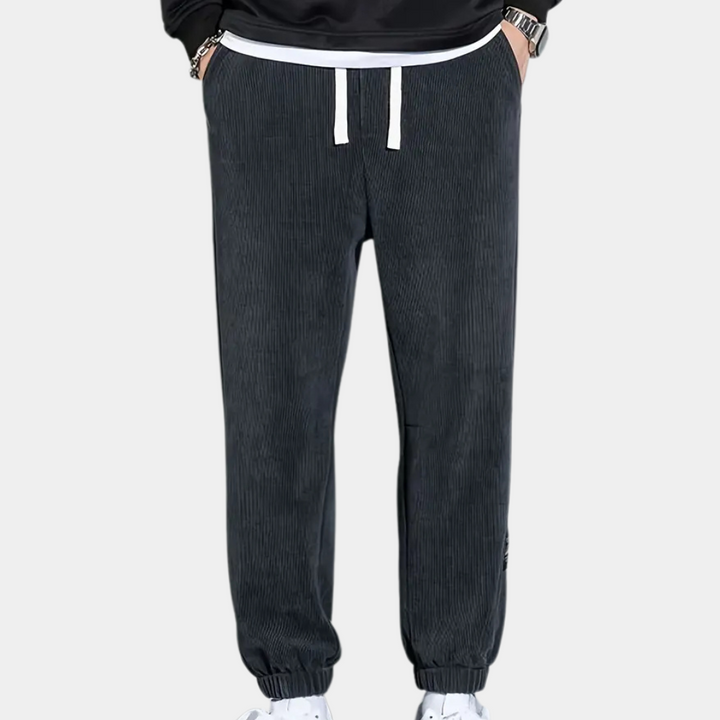 Donkergrijze corduroy joggingbroek voor heren met witte trekkoorden en elastische enkels, ideaal voor casual en sportieve outfits.