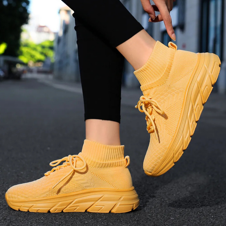 Gele hoge sneakers met dikke zool, gedragen door persoon in zwarte legging op straat. Modieuze dames sportschoenen, comfortabele pasvorm.