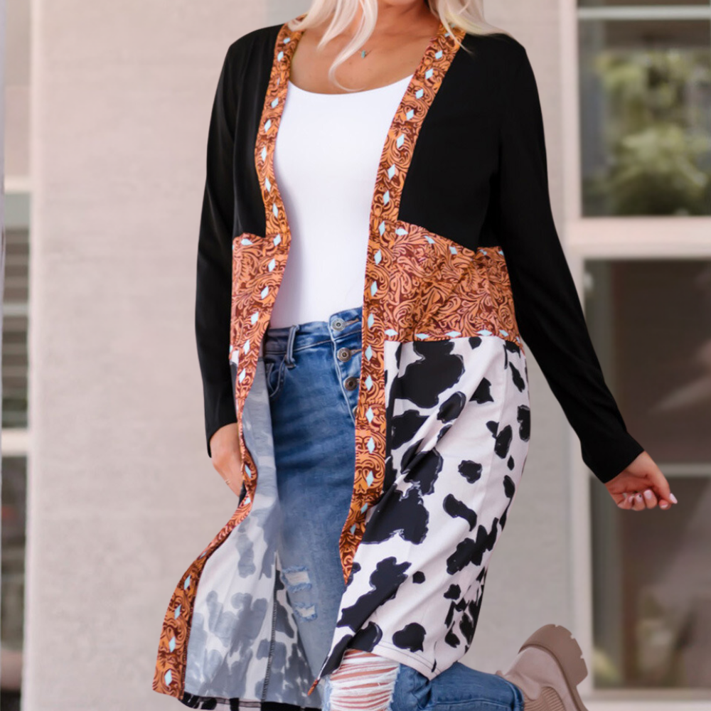Vrouw draagt stijlvolle lange cardigan met koeienprint en oranje paisley-patroon, gecombineerd met blauwe jeans en witte top. Modieuze dameskleding.