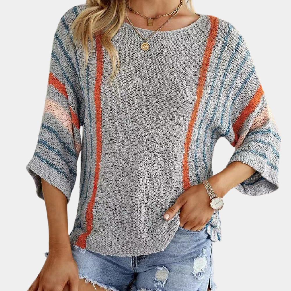 Grijze gebreide damestrui met kleurrijke strepen, driekwart mouwen en ronde hals, gecombineerd met denim shorts. Modieuze casual outfit.