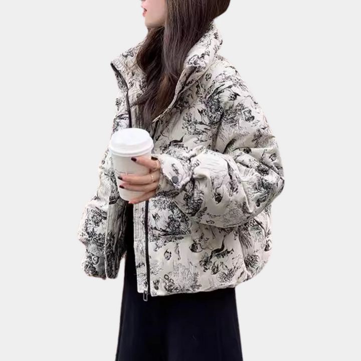 Vrouw in modieuze gewatteerde jas met zwart-wit bloemenprint, houdt een koffiebeker vast. Trendy winterkleding, casual stijl.
