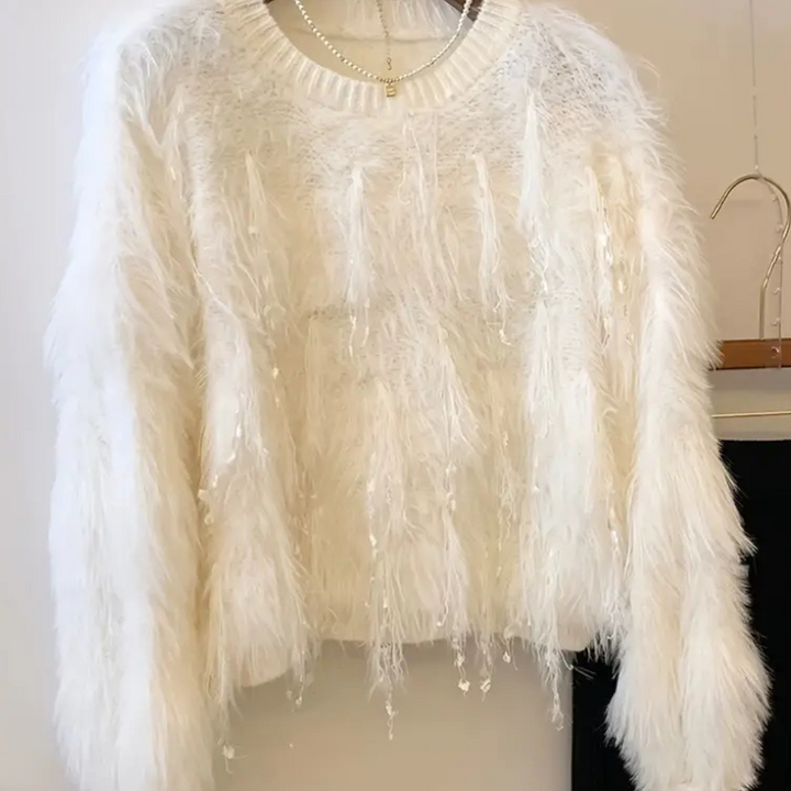 Witte pluizige trui met lange mouwen, versierd met glinsterende pailletten, hangend aan een hanger. Perfect voor wintermode en feestelijke gelegenheden.