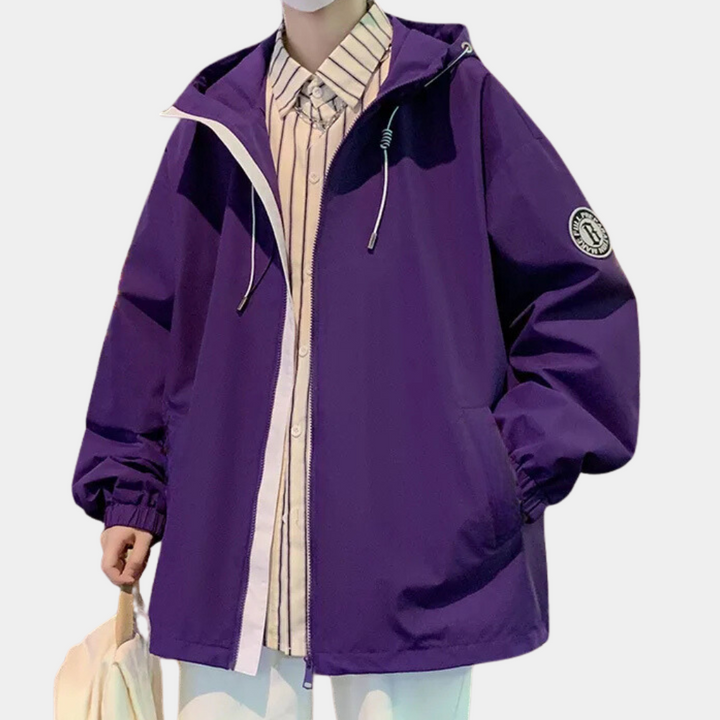 Paarse oversized jas met capuchon, ritssluiting en embleem op mouw, gedragen over gestreept overhemd. Modieuze unisex streetwear.