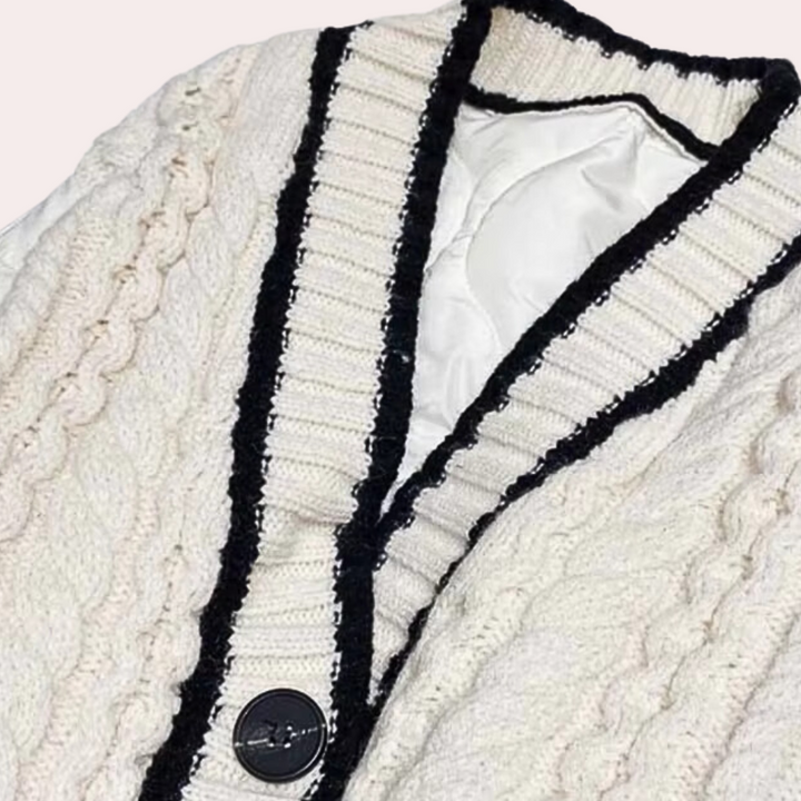 Crèmekleurig kabelgebreid vest met zwarte randen en knoopsluiting, stijlvolle wintermode, warme dameskleding, trendy gebreide textuur.