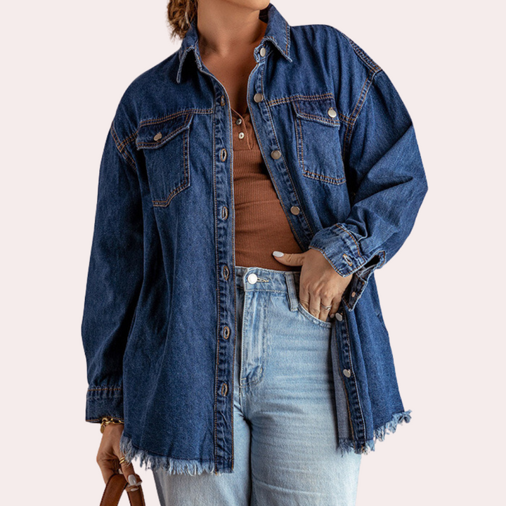 Vrouw draagt oversized denim spijkerjas met knopen, borstzakken en gerafelde zoom, gecombineerd met een bruine top en lichtblauwe jeans.