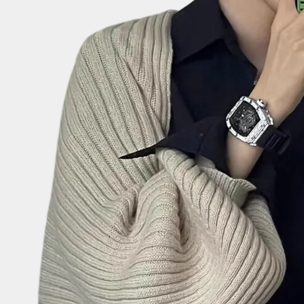 Persoon draagt een luxe horloge met zilveren kast en zwarte wijzerplaat, gecombineerd met een beige gebreide trui en zwarte blouse.