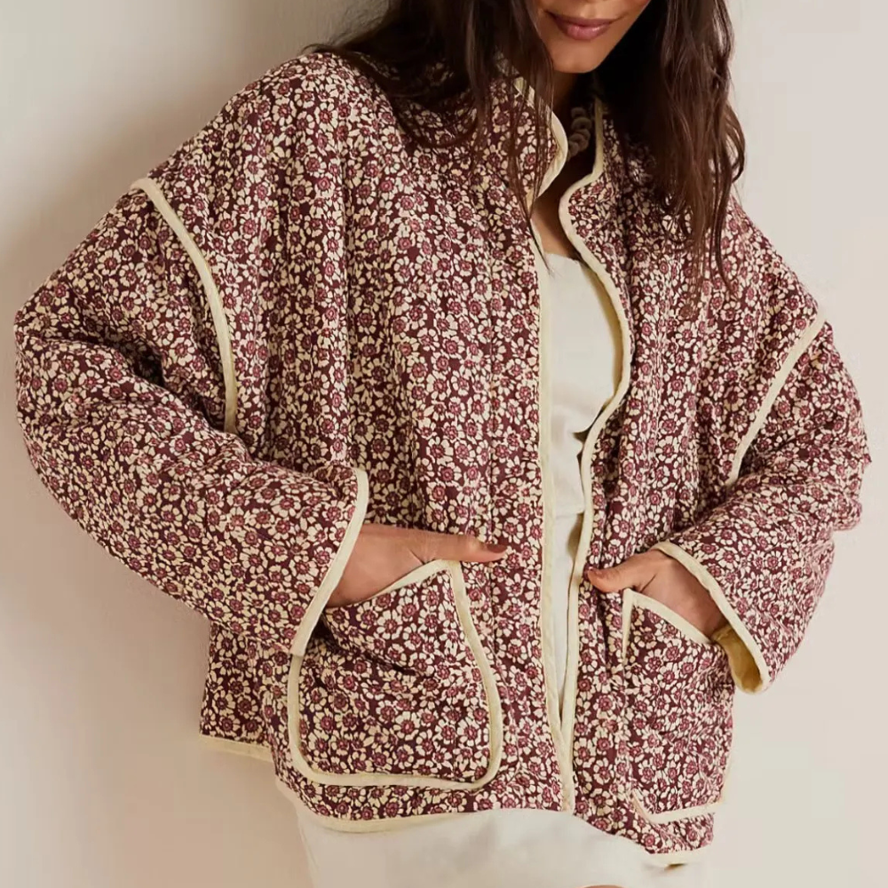 Vrouw draagt een bloemenjas met rode en witte print, beige biezen en grote zakken. Modieuze dameskleding, herfststijl, casual outfit.