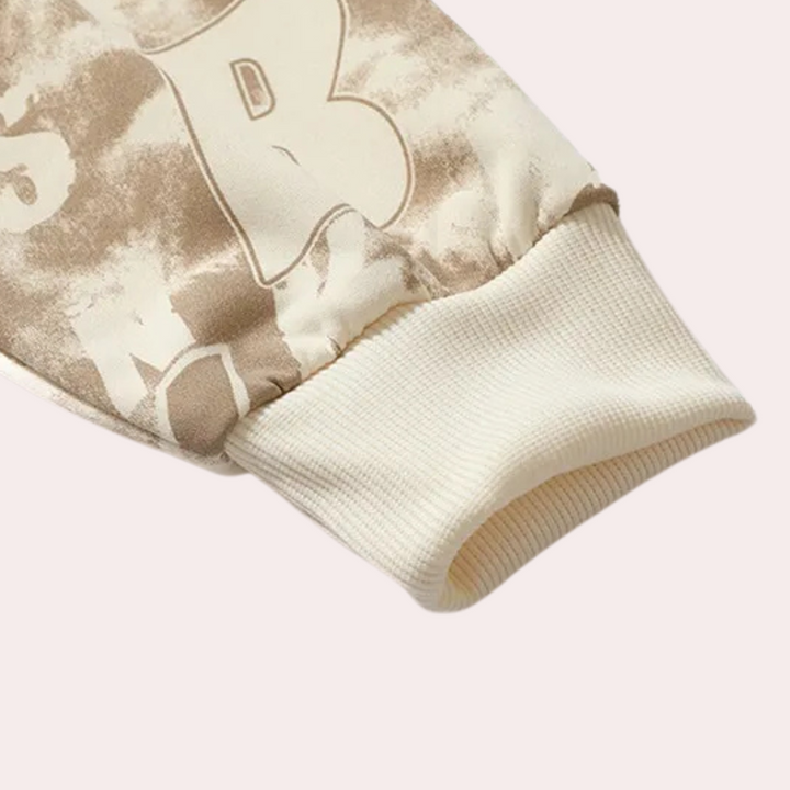 Beige en witte sweatshirtmouw met ribgebreide manchetten, tie-dye patroon en grote letters. Modieuze streetwear, comfortabele pasvorm.