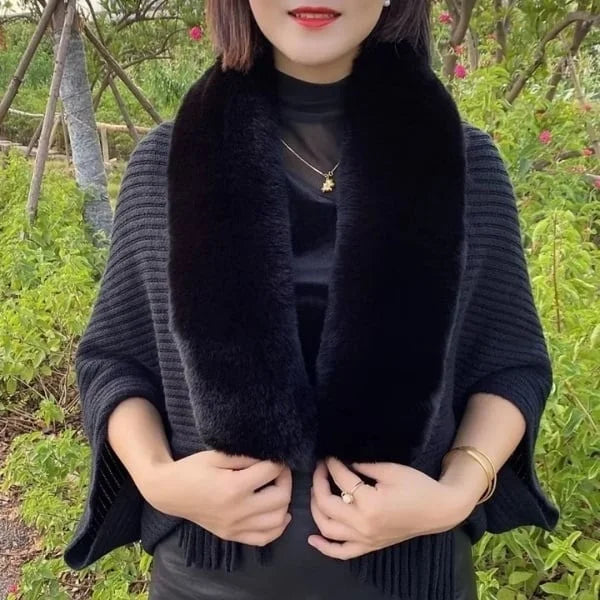 Vrouw draagt zwarte gebreide sjaal met bontkraag, elegante outfit, buiten in groene tuin. Modieuze herfst- of winterkledingaccessoire.