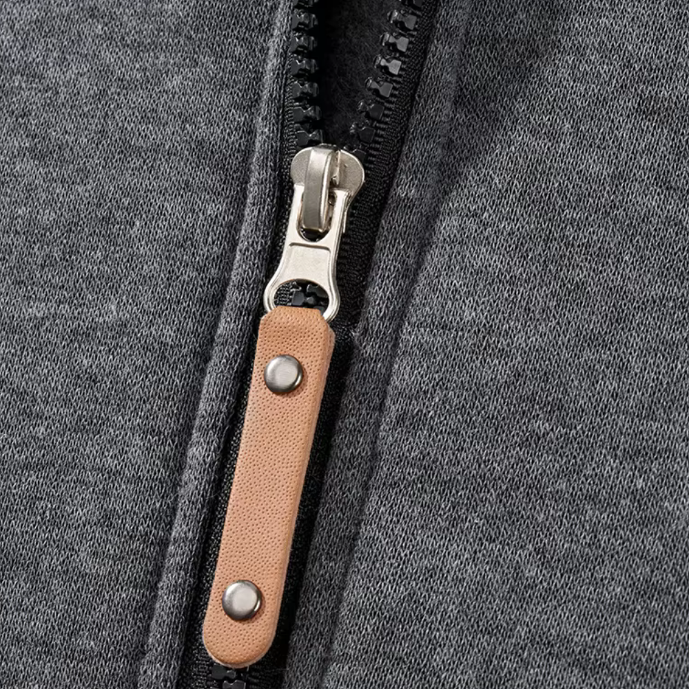 Grijze hoodie met ritssluiting en bruine leren ritstrekker, close-up. Modieuze herenkleding, comfortabele casual stijl, hoogwaardige stof.