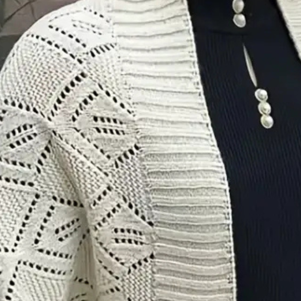 Witte gebreide cardigan met geometrisch patroon, gedragen over een zwarte top met parelknopen. Stijlvolle damesmode, herfstkleding.