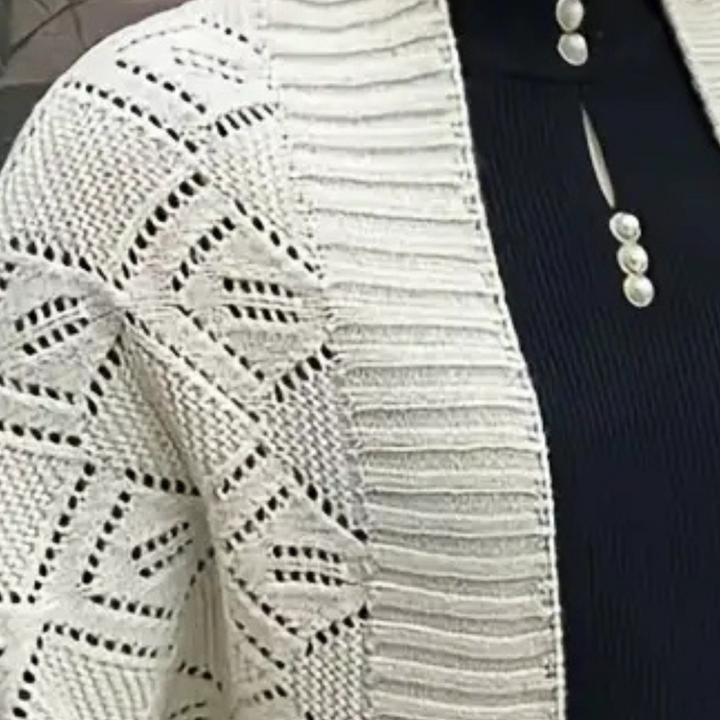 Witte gebreide cardigan met geometrisch patroon, gedragen over een zwarte top met parelknopen. Stijlvolle damesmode, herfstkleding.