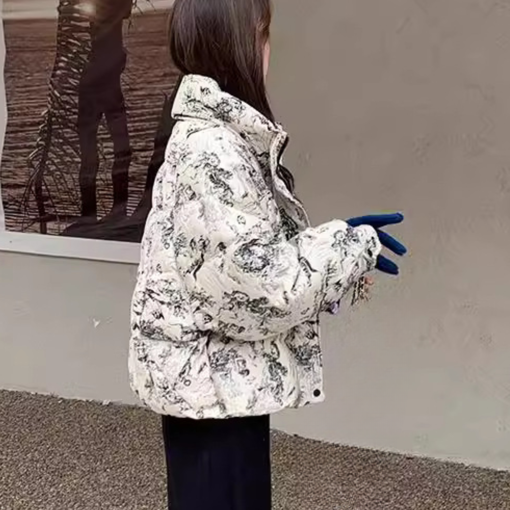 Dame in witte gewatteerde jas met bloemenprint, blauwe handschoenen, staand voor een grijze muur. Wintermode, trendy dameskleding, buitenkleding.