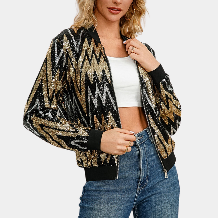 Vrouw draagt glinsterend zwart-goud bomberjack met zigzagpatroon, witte crop top en blauwe jeans. Modieuze dameskleding, trendy jassen.