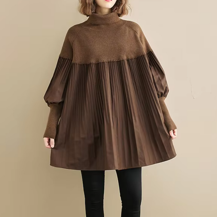 Vrouw draagt bruine oversized trui met geplooide details, lange mouwen en coltrui, gecombineerd met zwarte leggings. Modieuze herfstkleding.