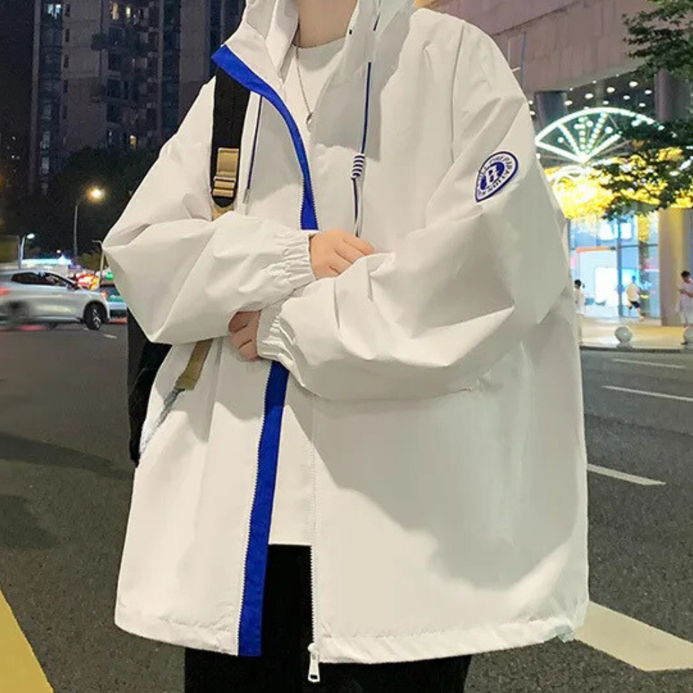 Witte oversized windjack met blauwe rits en capuchon, gedragen door persoon op straat 's avonds. Trendy streetwear, casual mode, stedelijke stijl.