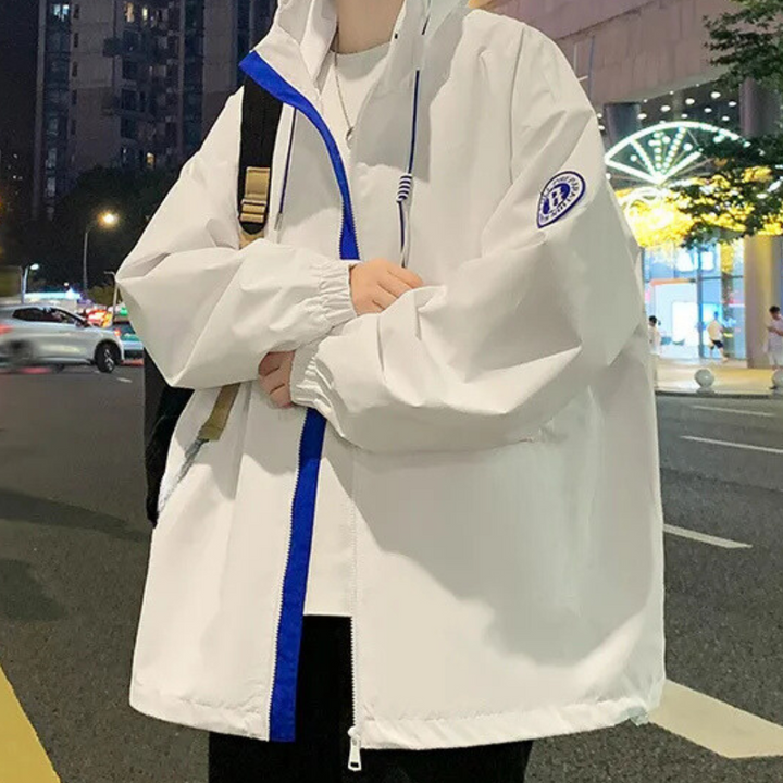 Witte oversized windjack met blauwe rits en capuchon, gedragen door persoon op straat 's avonds. Trendy streetwear, casual mode, stedelijke stijl.