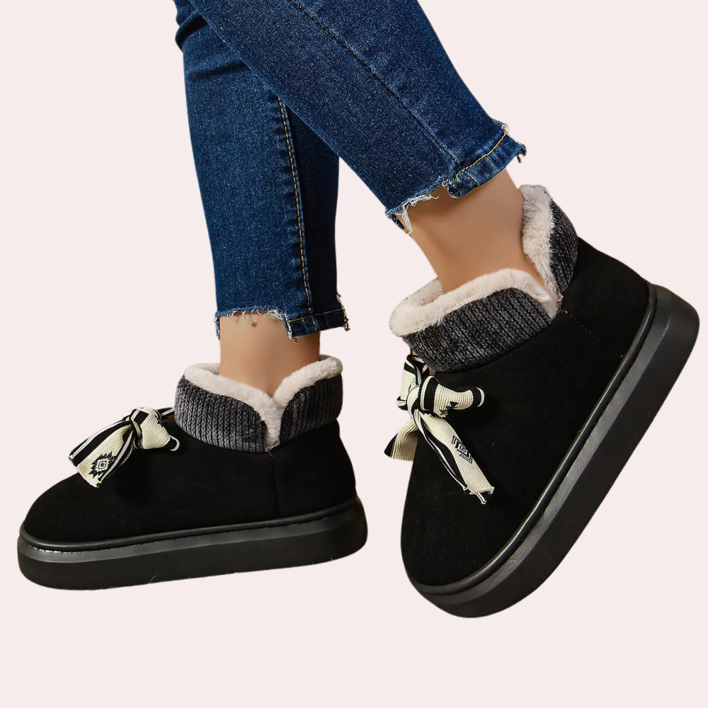 Zwarte dameslaarzen met bontvoering en strikdetail, gedragen met blauwe jeans. Warme winterlaarzen, comfortabele schoenen, modieuze dameskleding.