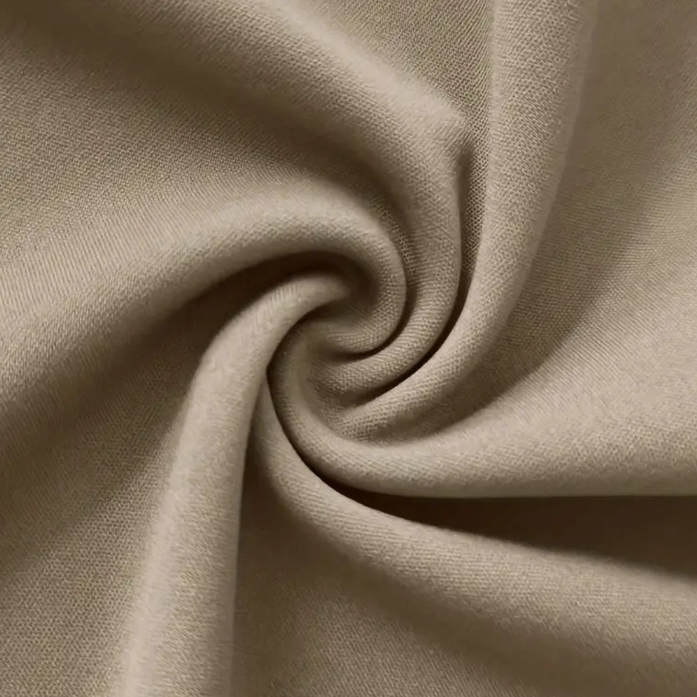 Beige katoenen stof close-up, gedraaid in een spiraalpatroon. Zachte textuur, ideaal voor kleding en interieurdecoratie. Hoogwaardige textielmaterialen.