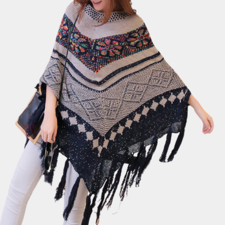 Vrouw draagt kleurrijke gebreide poncho met etnisch patroon en franjes, perfect voor herfstmode. Stijlvol en warm, ideaal voor casual outfits.