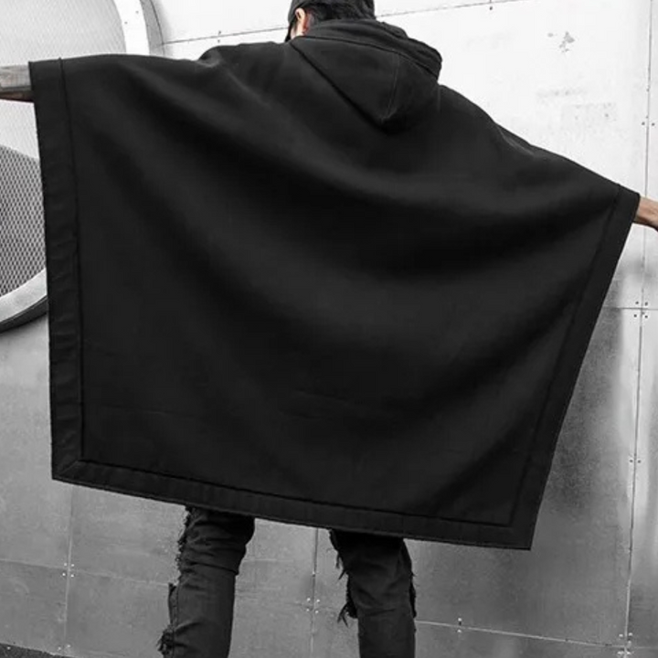 Man in zwarte poncho met capuchon, rugaanzicht. Stijlvolle streetwear, urban mode, minimalistisch ontwerp. Geschikt voor herfst- en winterseizoen.