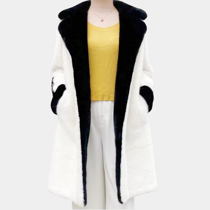 Witte damesjas met zwarte kraag en voering, gecombineerd met gele trui en witte broek. Stijlvolle wintermode, elegant en warm.