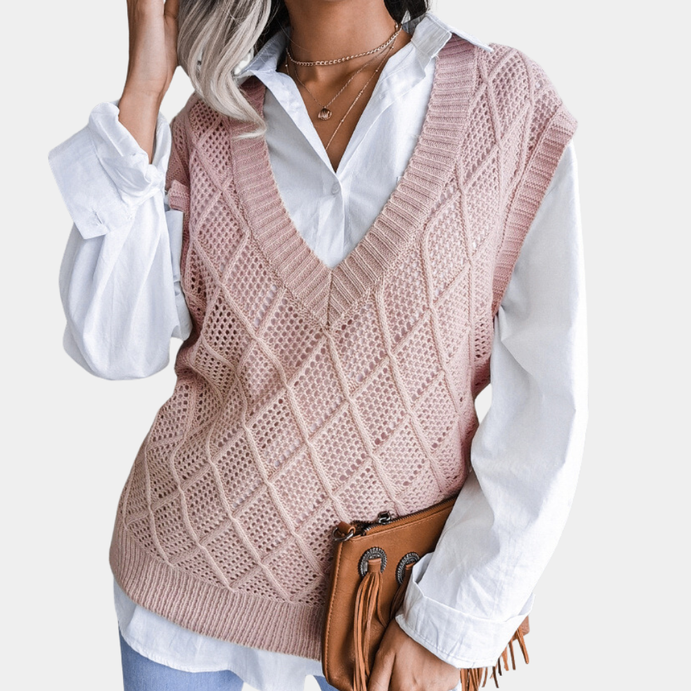 Vrouw in roze gebreide spencer met ruitpatroon, witte blouse en blauwe jeans, houdt bruine leren tas vast. Modieuze dameskleding herfst 2023.