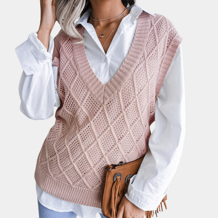 Vrouw in roze gebreide spencer met ruitpatroon, witte blouse en blauwe jeans, houdt bruine leren tas vast. Modieuze dameskleding herfst 2023.
