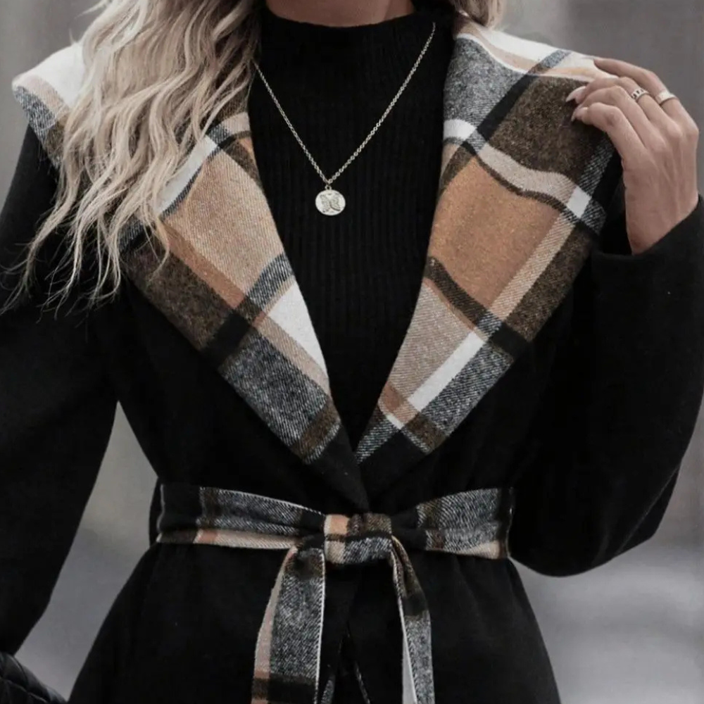Vrouw in zwarte jas met geruite kraag en riem, gouden ketting, modieuze herfstkleding, stijlvolle damesmode, trendy outfit voor koud weer.