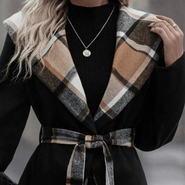 Vrouw in zwarte jas met geruite kraag en riem, gouden ketting, modieuze herfstkleding, stijlvolle damesmode, trendy outfit voor koud weer.