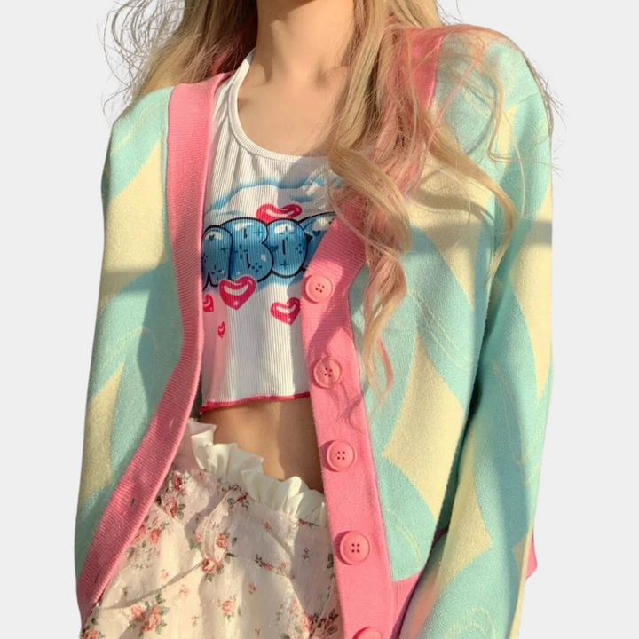 Vrouw in pastel cardigan met roze knopen, wit crop top met blauwe tekst, en bloemenrok. Trendy damesmode, kleurrijke kledingstijl.