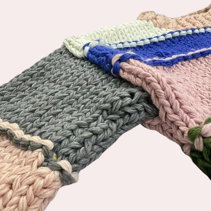 Grofgebreide deken in pastelkleuren, met dikke garens in grijs, roze en blauw. Perfect voor interieurdecoratie en warme, gezellige sferen.