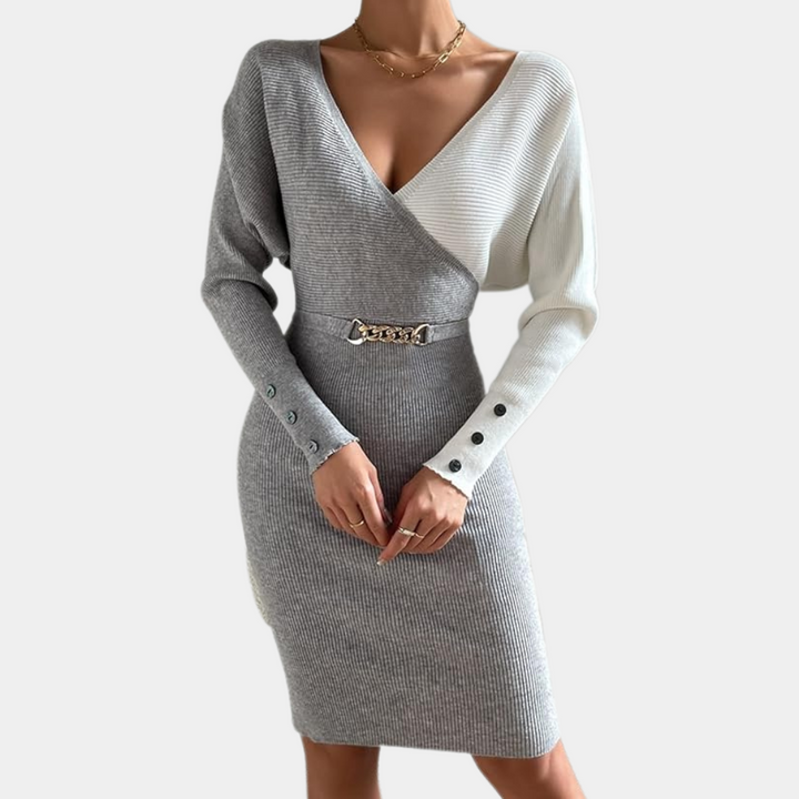 Grijze en witte gebreide jurk met V-hals en lange mouwen, voorzien van een riem met kettingdetail. Elegante damesmode, herfst/winter outfit.