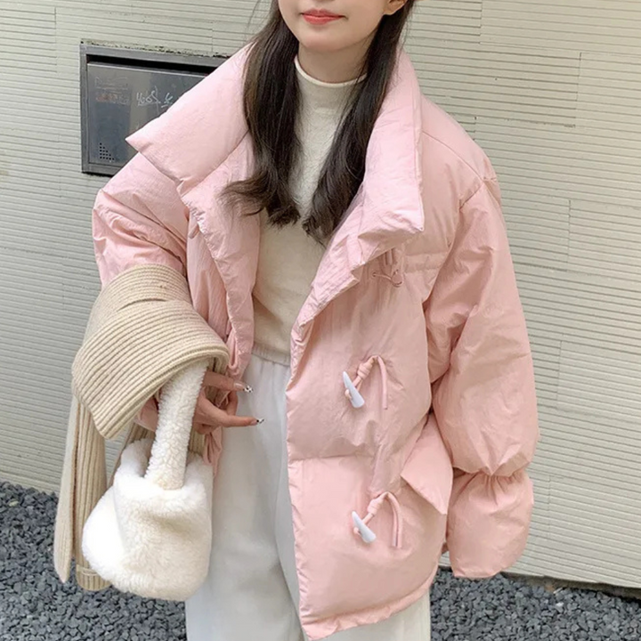 Vrouw in roze gewatteerde jas met grote kraag, witte broek en crèmekleurige sjaal. Wintermode, trendy dameskleding, casual stijl.