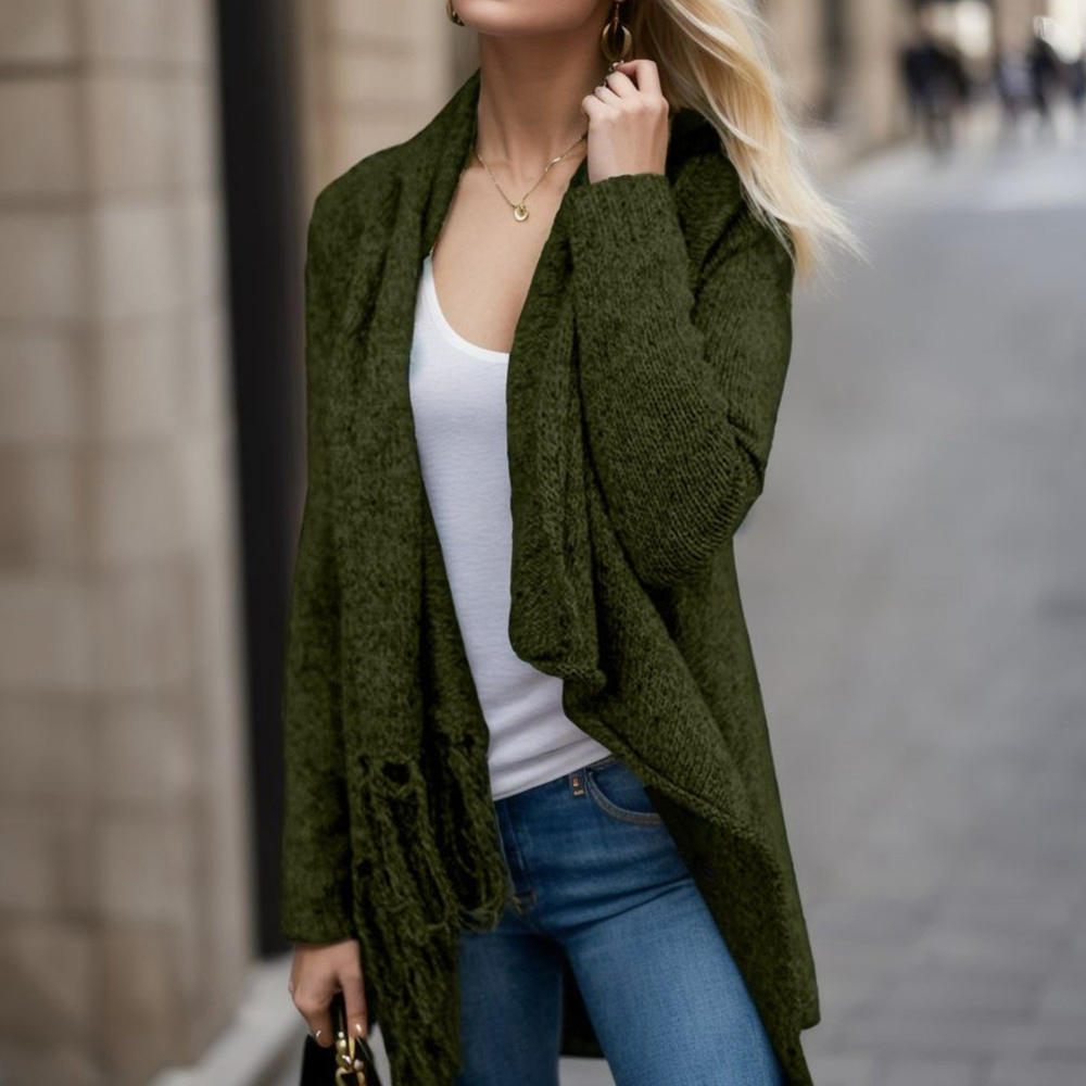 Vrouw in groene gebreide cardigan, witte top en blauwe jeans, wandelend in stedelijke omgeving. Modieuze herfstkleding, casual damesoutfit.