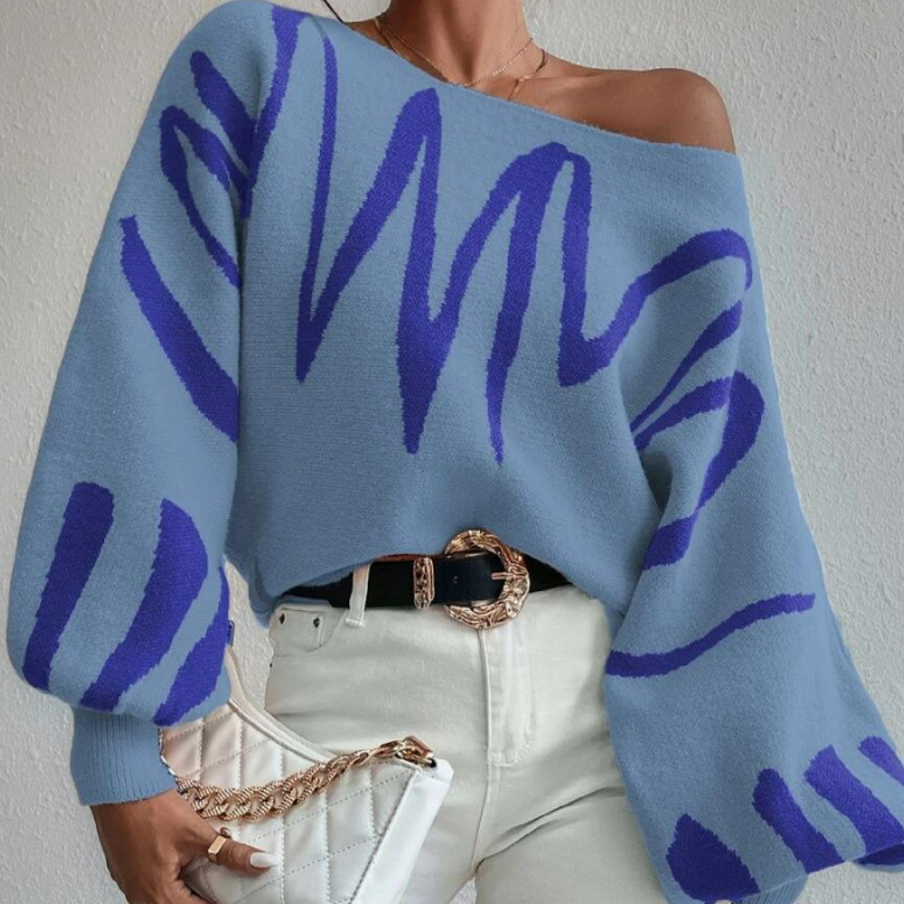 Vrouw draagt blauwe trui met abstracte paarse strepen, gecombineerd met witte broek en gewatteerde tas. Modieuze dameskleding, herfststijl.