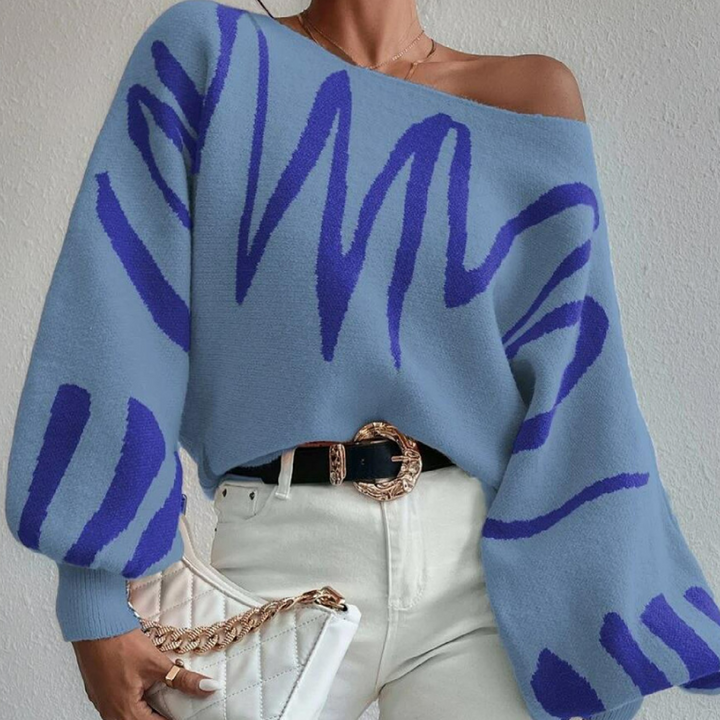 Vrouw draagt blauwe trui met abstracte paarse strepen, gecombineerd met witte broek en gewatteerde tas. Modieuze dameskleding, herfststijl.