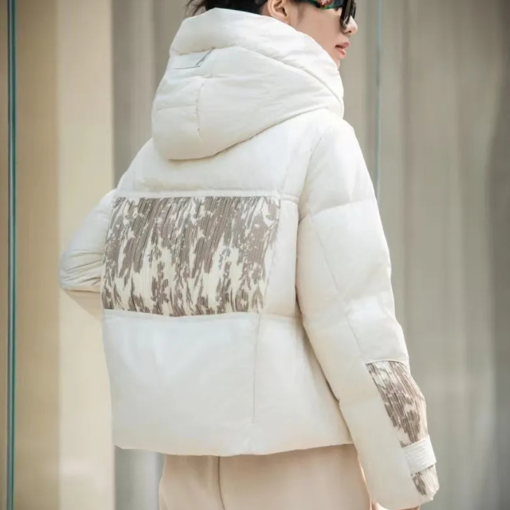 Witte gewatteerde winterjas met capuchon en beige patroon op de rug en mouwen, gedragen door een model. Stijlvolle damesmode, warme winterkleding.
