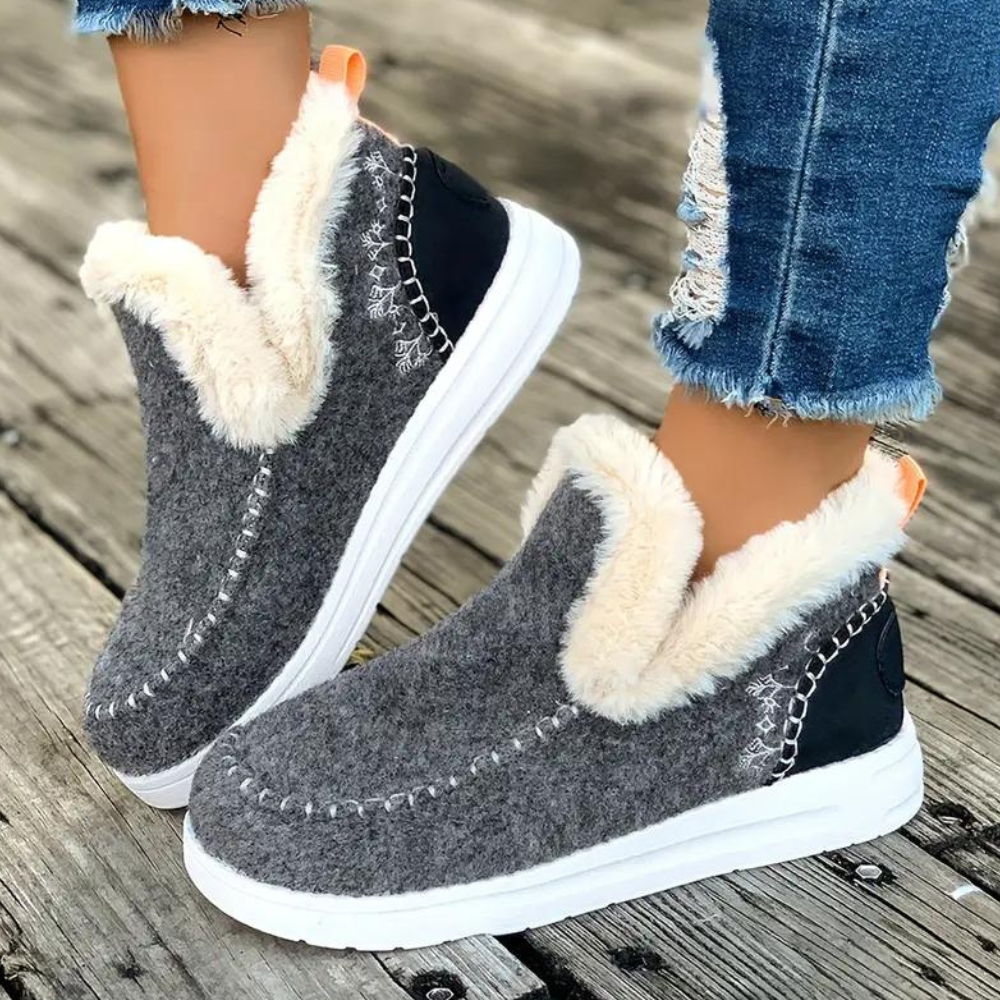 Grijze dameslaarzen met witte zool en warme voering, gedragen met gescheurde jeans op houten vloer. Comfortabele wintermode, trendy schoenen.