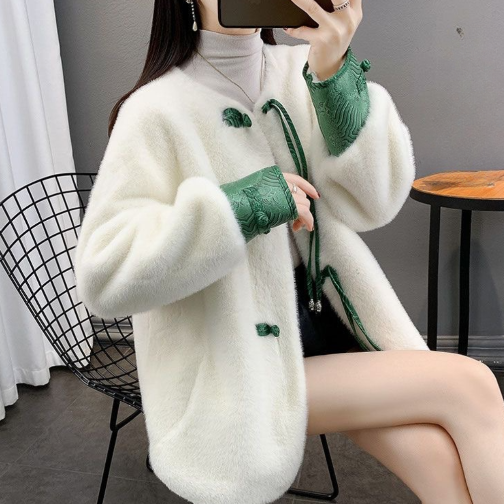 Vrouw in witte wollen jas met groene details, zittend op een moderne stoel. Stijlvolle wintermode, elegant design, trendy dameskleding.