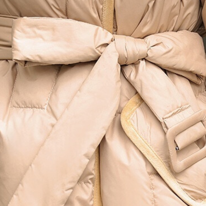 Beige gewatteerde winterjas met ceintuur, close-up van strik en gesp. Modieuze damesjas, warme winterkleding, stijlvolle buitenkleding.
