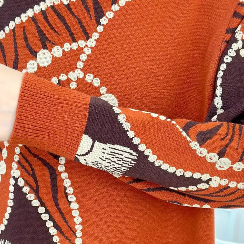 Oranje en bruine trui met abstract patroon en parelprint, close-up van mouw. Modieuze herfstkleding, warme gebreide stof, trendy design.