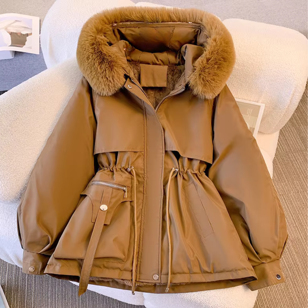 Bruine winterjas met bontkraag, verstelbare taille en zakken, liggend op een stoel. Stijlvolle damesjas, perfect voor koude seizoenen.