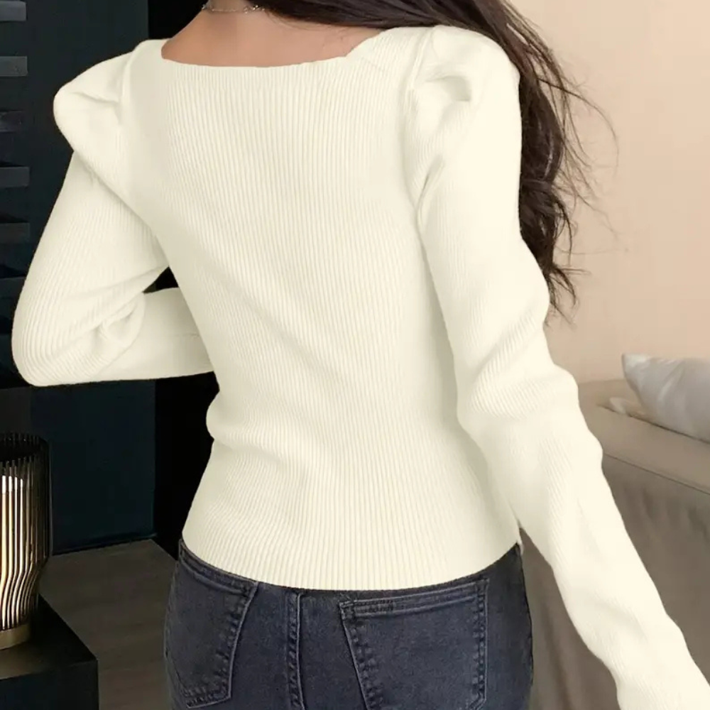 Vrouw in crèmekleurige ribgebreide trui met lange mouwen en pofschouders, gecombineerd met donkerblauwe jeans. Trendy damesmode, herfststijl.