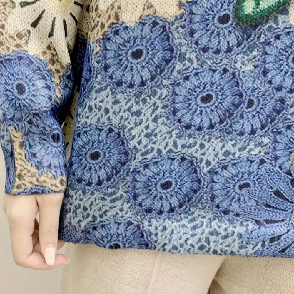 Blauwe gebreide trui met bloemmotief, close-up van mouw en hand. Modieuze dameskleding, herfst-winter collectie, comfortabele en stijlvolle outfit.